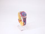 une montre colorée posée sur un socle transparent, sur une surface blanche