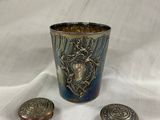 une tasse plaquée argent et deux boutons en argent sur un tissu blanc