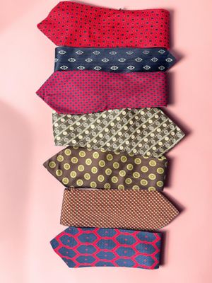 six different colored ties arranged in a row on a pink background