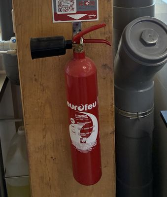 un extincteur fixé au mur à côté d'une borne d'incendie