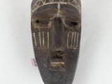 an old wooden mask hanging on a wall on a white surface