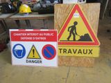 deux panneaux d'avertissement posés au sol, à côté d'un panneau de chantier