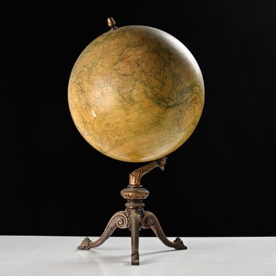 an antique globe on a tripod stand against a black background