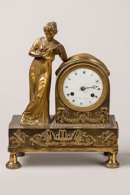 a gold clock with a woman standing next to it