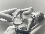 a nude woman laying on a bed with a fish bowl