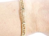 someone is wearing a gold bracelet with a greek design on it