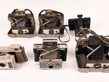 several old cameras are lined up in a row on a white surface
