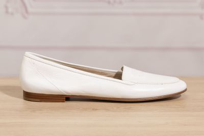 the white loafer is on a wooden table with a pink wall in the background
