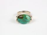 un gros plan d'une bague sertie d'une pierre turquoise sur une surface blanche