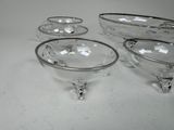 four clear glass bowls with silver rims on a white surface