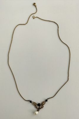 a gold necklace with a pearl and black beads on a white background
