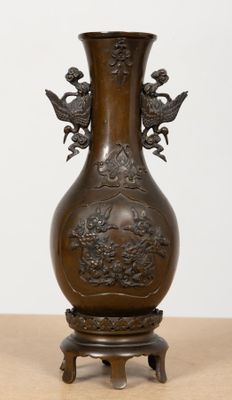 un vase en bronze posé sur un socle en bois, lui-même posé sur une table