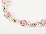 a close up of a pink and gold beaded necklace on a white surface