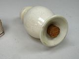 a white vase with a cookie in it next to a miniature house
