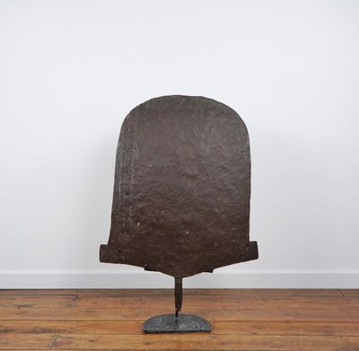 un vieux casque en fer posé sur un socle métallique, sur un plancher en bois