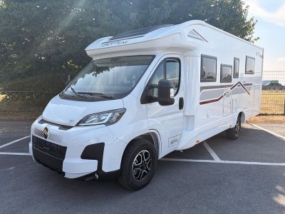 un camping-car blanc garé sur un parking, avec des arbres en arrière-plan