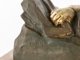 bronze statue of a man reading a book on a rock