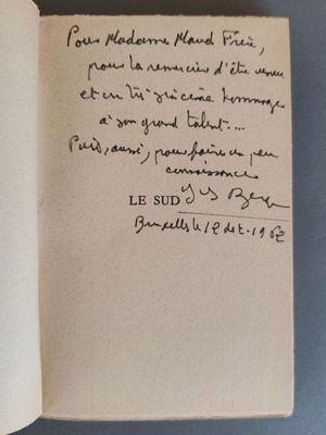un livre ouvert, sur lequel est inscrit un poème manuscrit, posé sur une table