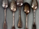 five silver spoons are lined up on a gray surface