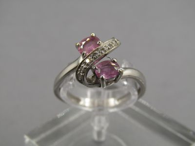 un gros plan d'une bague sertie d'un saphir rose et de diamants, posée sur un socle transparent