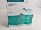 une boîte vide contenant une brosse à dents, posée sur une surface blanche