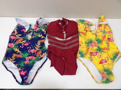 Trois maillots de bain sont alignés sur une table blanche
