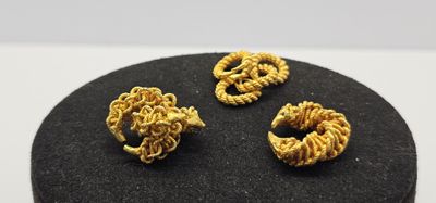 trois bijoux de couleur dorée posés sur une surface noire