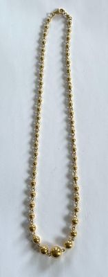 un gros plan d'un collier de perles dorées posé sur une surface blanche