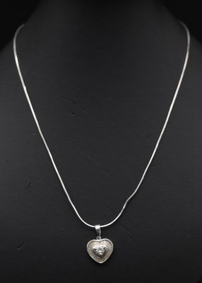 un pendentif en forme de cœur en argent, suspendu à une chaîne en argent, sur un mannequin