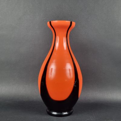 un vase orange et noir posé sur une surface grise
