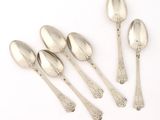 five silver spoons and a spoon with a spoon handle on a white surface