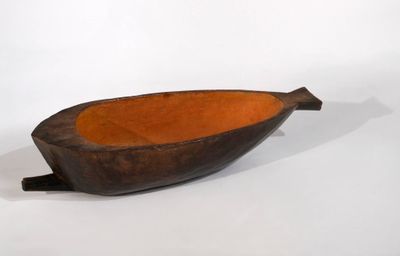 une image représentant un bol en forme de bateau en bois posé sur une surface blanche