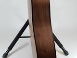 an acoustic guitar sits on a tripod stand against a white background