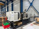 une photo montrant une grande machine dans un entrepôt, avec des cartons posés par terre