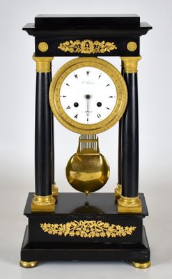 une horloge noire et dorée posée sur un socle, sur fond blanc