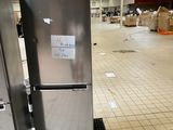 un réfrigérateur argenté posé dans un entrepôt, avec des cartons par terre