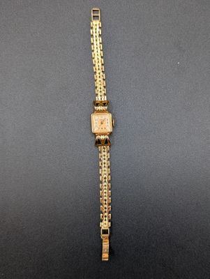 une image représentant une montre en or posée sur une surface noire