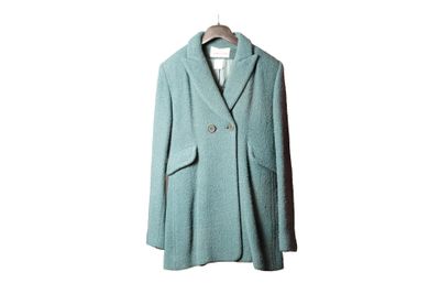un manteau en laine suspendu à un cintre, lui-même accroché à un mur blanc