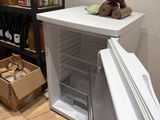 un petit réfrigérateur dans un coin d'une pièce où se trouvent des cartons par terre