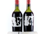 two bottles of red wine sitting next to each other on a white surface