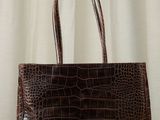 a brown crocodile skin handbag sitting on top of a wooden table