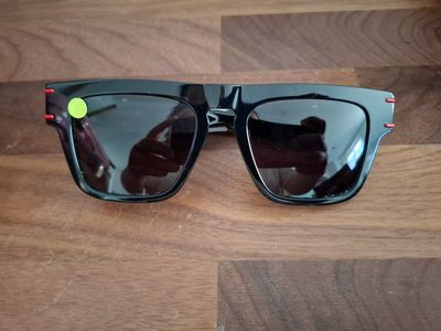 des lunettes de soleil posées sur une table en bois, avec une personne en train de prendre une photo