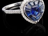 une bague en saphir bleu et diamants en forme de cœur, posée sur un fond noir