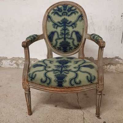 une vieille chaise dont l'assise est recouverte d'un tissu bleu et vert