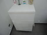 a white chest of drawers in the corner of a bathroom