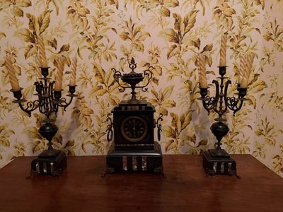 three candles and a clock on a table in front of a floral wallpaper