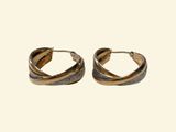 a pair of gold toned hoop earrings sitting on top of a white surface