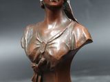 an antique bronze bust of a woman with a bird on her shoulder