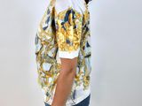 a woman wearing a white shirt with a gold and blue pattern on it