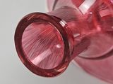 a pink glass vase with a red handle on a white table
